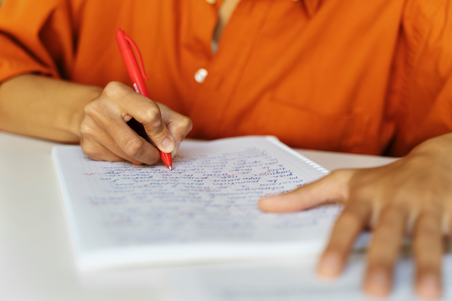 A close-up photo of a person writing in a notebook, cropped to show only their hands and the notebook.